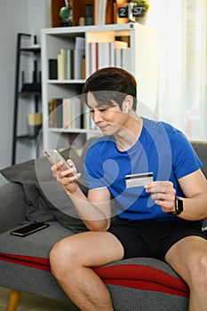 Portrait of asian man in casual clothes holding credit card, paying bill with online payment via internet on smart phone