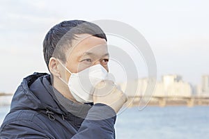 Portrait of an Asian man in mask who coughs against the background of the city and the river