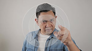 Portrait of Asian man showing cynical unhappy angry facial expression pointing forward, giving warn