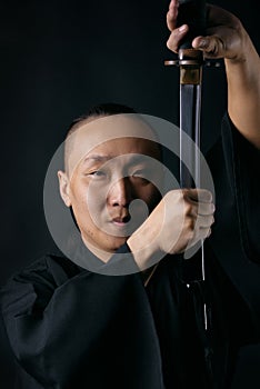 Portrait of an Asian man with a sword in hands on a black background, a samurai.