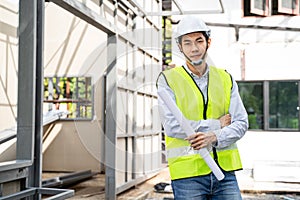 Portrait of Asian man worker stand with arm crossing onsite of architecture building and structure. Male engineers holding drawing