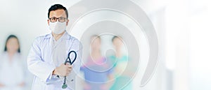 Portrait of Asian medical male Doctor wear a mask to prevent germs and standing in front of his blurred team staff in hospital