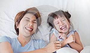 Portrait of asian mom and little daughter are cuddling and smiling in white bed room, close up happy face of asian family.