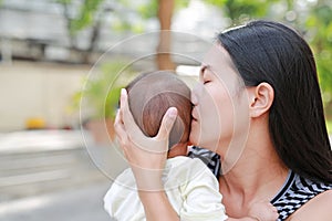 Portrait of Asian mother carrying and kissing her infant baby boy outdoor