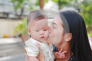 Portrait of Asian mother carrying and kissing her infant baby boy outdoor