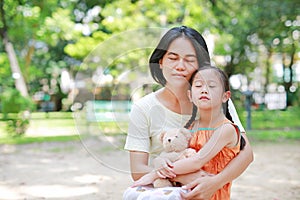 Portrait of Asian mother cuddle daughter and hugging teddy bear doll in the garden. Mom and child girl with love and relationship