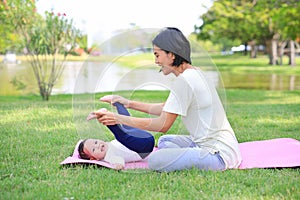 Portrait of Asian mother doing baby yoga for her son on green lawn in the nature garden outdoor