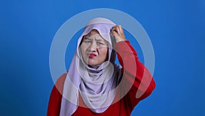 Portrait of Asian muslim woman shows refusal or denial gesture, shoulder shrug, I don`t know expression, against red background