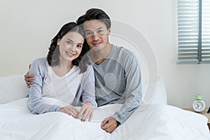 Portrait of Asian new marriage couple laying on bed and look at camera. Attractive beautiful young man and woman in pajamas enjoy