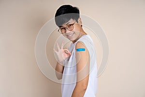 Portrait of Asian people showing his shoulder with blue bandage after getting vaccine on isolated background. She is happy and