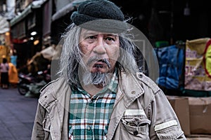 Portrait of Asian poor homeless man standing on side of city street. Addiction aged man with white beard and hair wandering on