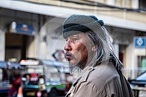 Portrait of Asian poor homeless man standing on side of city street. Addiction aged man with white beard and hair wandering on