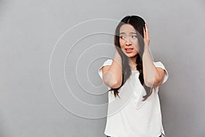 Portrait of asian puzzled woman 20s in white t-shirt touching he