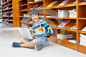 Portrait of Asian school boy in casual shirt with laptop computer in Public Library, Schooling and Learning by Computer Concept