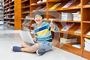 Portrait of Asian school boy in casual shirt with laptop computer in Public Library, Schooling and Learning by Computer Concept