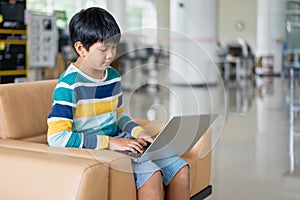 Portrait of Asian school boy in casual shirt with laptop computer in Public Library, Schooling and Learning by Computer Concept