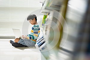 Portrait of Asian school boy in casual shirt with laptop computer in Public Library, Schooling and Learning by Computer Concept