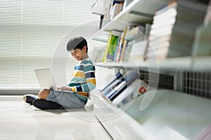 Portrait of Asian school boy in casual shirt with laptop computer in Public Library, Schooling and Learning by Computer Concept