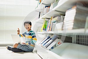 Portrait of Asian school boy in casual shirt with laptop computer in Public Library, Schooling and Learning by Computer Concept