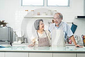 Portrait of Asian Senior elderly Couple wear apron in kitchen at home. Happy Loving Older Grandfather hug grandmother with