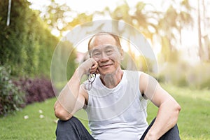 Portrait of Asian senior man relaxing and sitting on grass at th