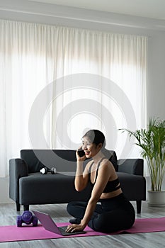 Portrait asian sporty woman in sportswear working out and using laptop and call phone at home in living room, sitting on