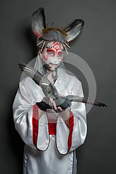 Portrait of asian style woman with Halloween makeup and carnival mask holding bird pigeon on black background