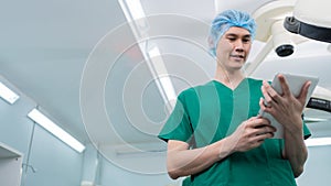 Portrait of Asian surgeon with medical mask standing and holding a tablet in operation theater at a hospital. Team of Professional