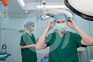 Portrait of Asian surgeon with medical mask standing in operation theater at a hospital. Team of Professional surgeons. Healthcare