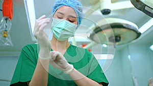 Portrait of Asian surgeon with medical mask standing and wearing medical gloves in operation theater at a hospital. Team of