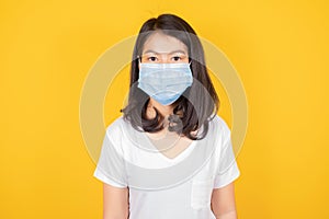 Portrait of Asian teenager  in medical face mask to protect Covid-19 Coronavirus wears white t-shirt on yellow background,