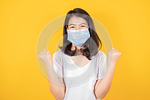 Portrait of Asian teenager  in medical face mask to protect Covid-19 Coronavirus wears white t-shirt on yellow background,