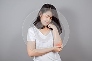 Portrait of Asian teenager wears white t-shirt having pain in injured elbow on gray