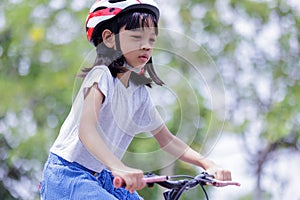 Portrait of Asian Thai kid girl Cute and bright face, 6 to 8 years old, riding a red bicycle outdoors. She enjoys riding exercise