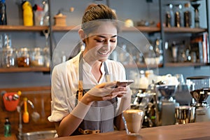 Portrait of Asian woman barista taking photo to coffee with smartphone for post to sell online on the internet or marketing social