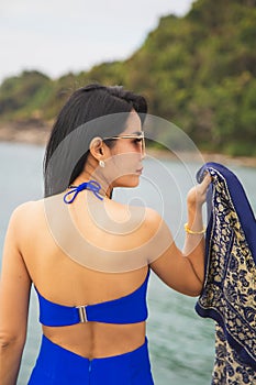 Portrait Asian woman in blue casual wear with a blue shawl, she is standing in front of the sea, summer lifestyle fashion concept