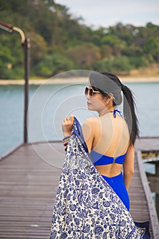 Portrait Asian woman in blue casual wear with a blue shawl, she is standing on the wooden bridge in front of the sea, summer