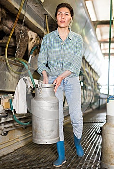 Portrait of a asian woman on a farm, passing by a milking machine, holding a milk flask