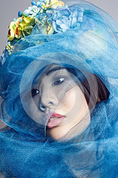 Portrait of asian woman with floral hat and blue veil looking aside on light grey background