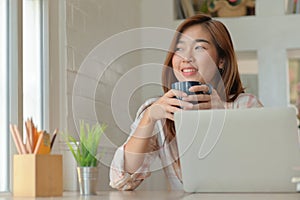 A portrait of a Asian woman happily smiles with a coffee cup during a break from working in a comfortable office
