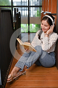 Portrait, Asian woman in a library, listening to music while reading a book