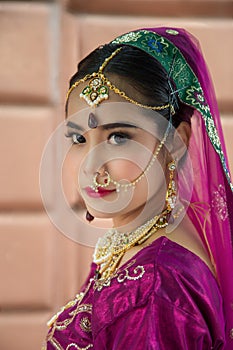 Portrait Asian woman in a margenta Indian tradition sari, she is looking at a camera next to the white wall