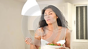 Portrait of asian woman in nightie eating salad in kitchen at home. Woman having healthy breakfast.