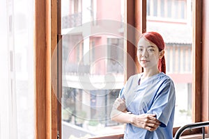 Portrait of Asian woman nurse wearing medical scrubs in the house of patient. Caregiver visit at home. Home health care.