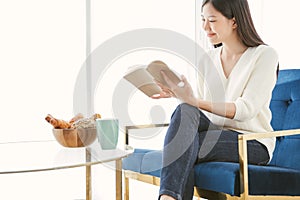 Portrait Asian woman reading book and relaxing with coffee at home.