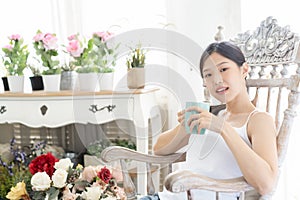 Portrait Asian woman relaxing on wooden chair with coffee at home.