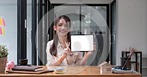 Portrait of Asian woman showing or presenting tablet computer with blank white screen, real estate working at office