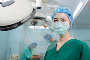 Portrait of Asian woman surgeon with medical mask standing in operation theater at a hospital. Team of Professional surgeons.