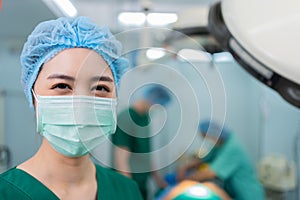 Portrait of Asian woman surgeon with medical mask standing in operation theater at a hospital. Team of Professional surgeons.