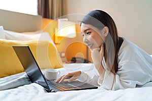 Portrait of Asian woman wearing bathrobe using a laptop on the bed